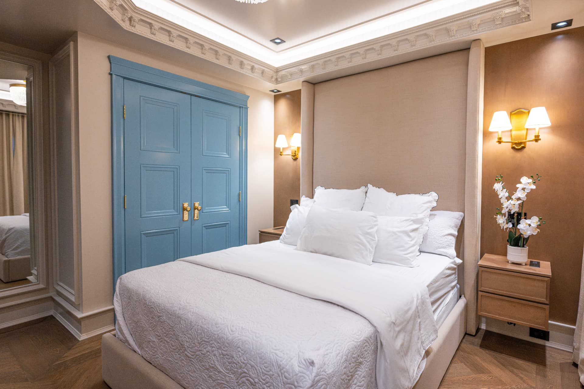 Bedroom with an upholstered headboard, white bedding, powder blue doors, and gold sconces