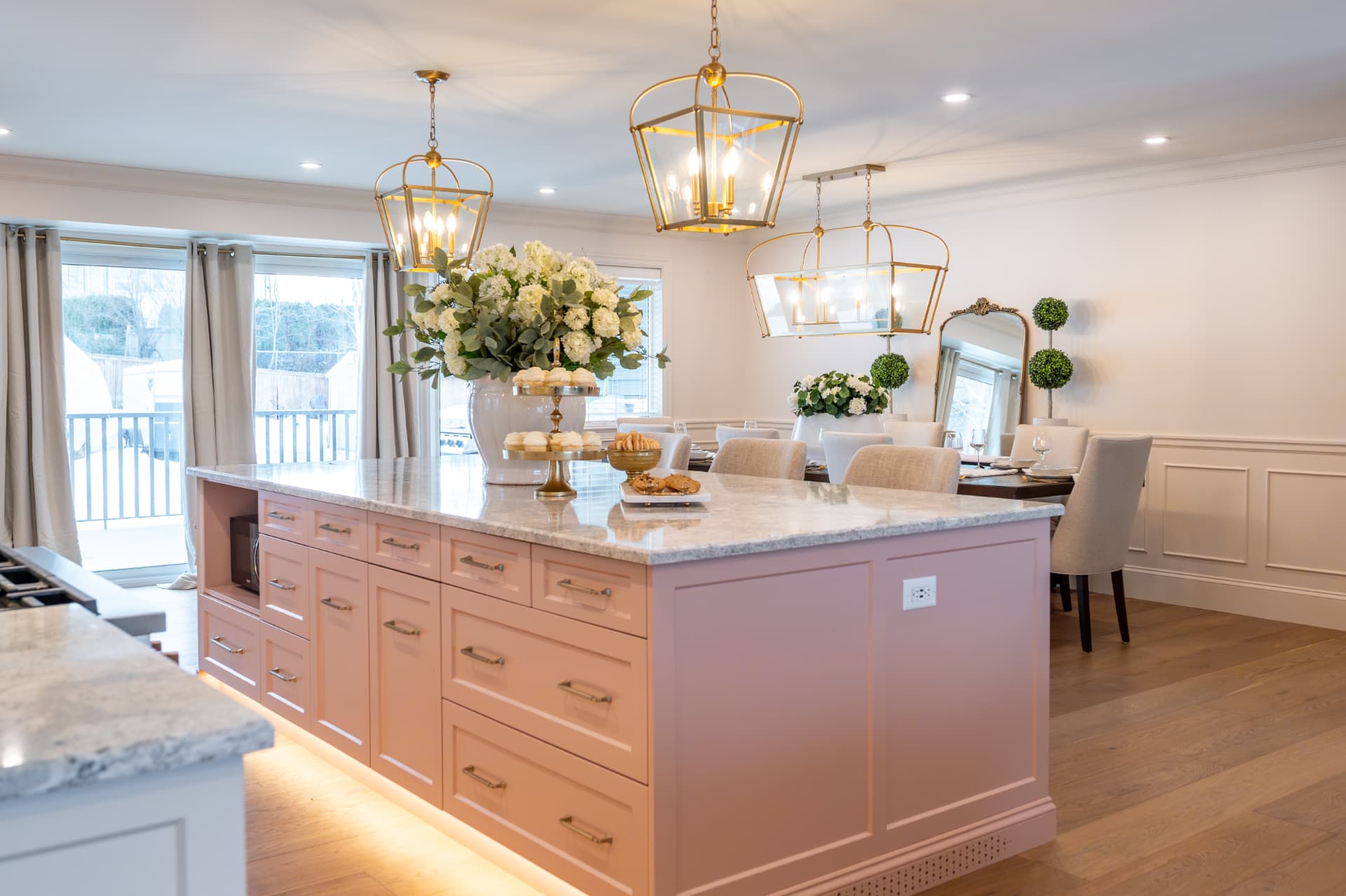 Open kitchen and dining space with a blush island, marble counters, and brass lantern pendants
