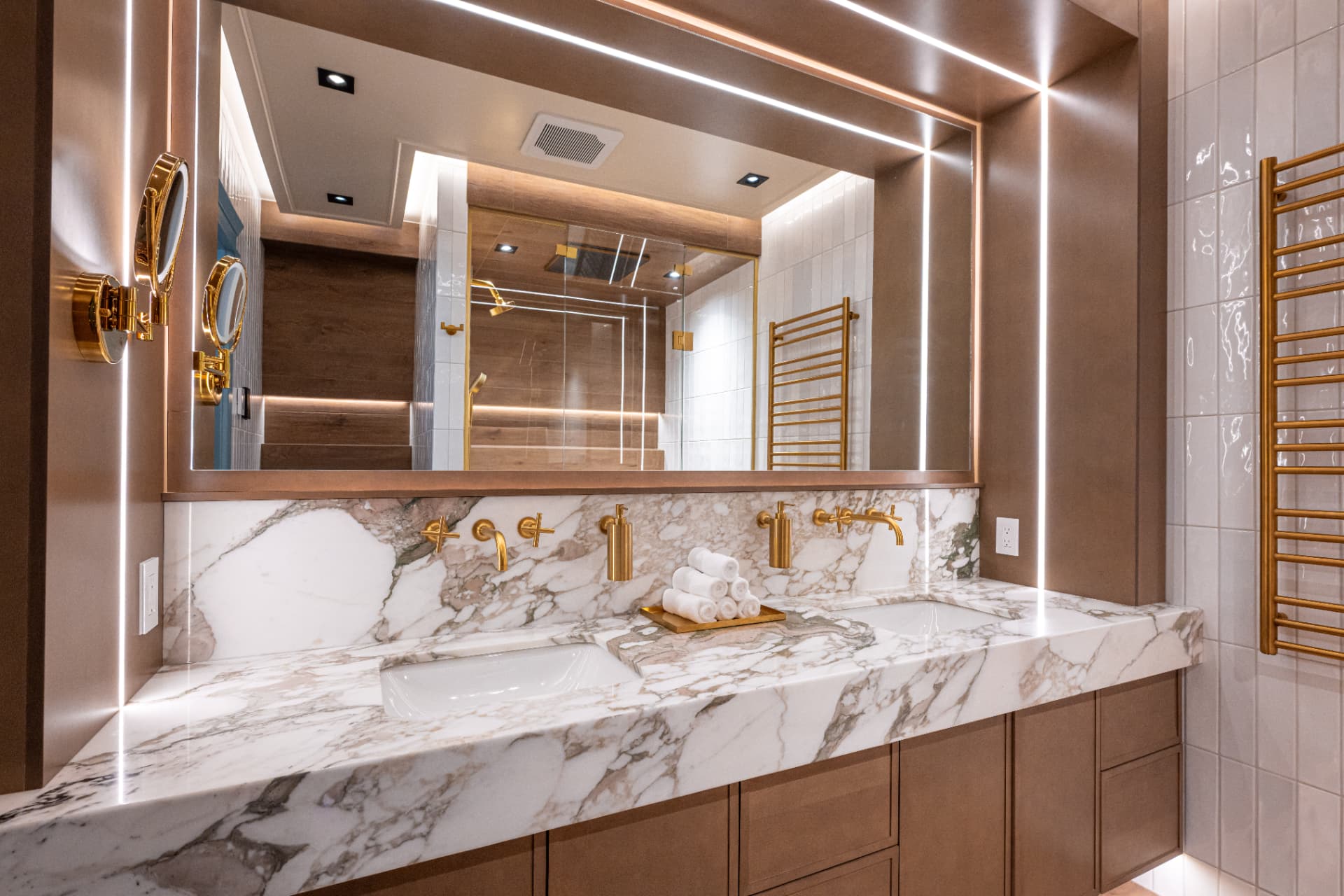 Marble double vanity with integrated lighting, bronze cabinetry, and brass fixtures