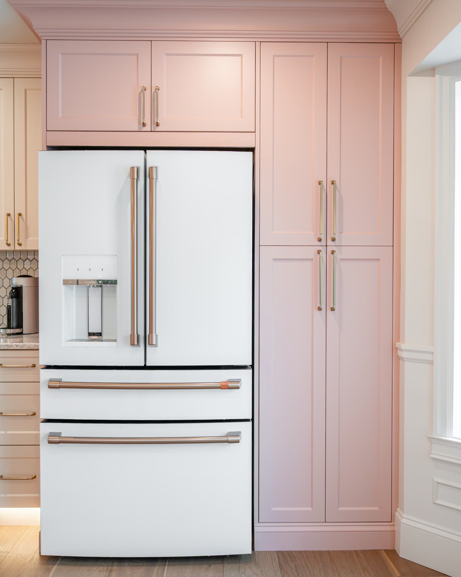 Integrated refrigerator within blush cabinetry finished with brass hardware and under-cabinet lighting