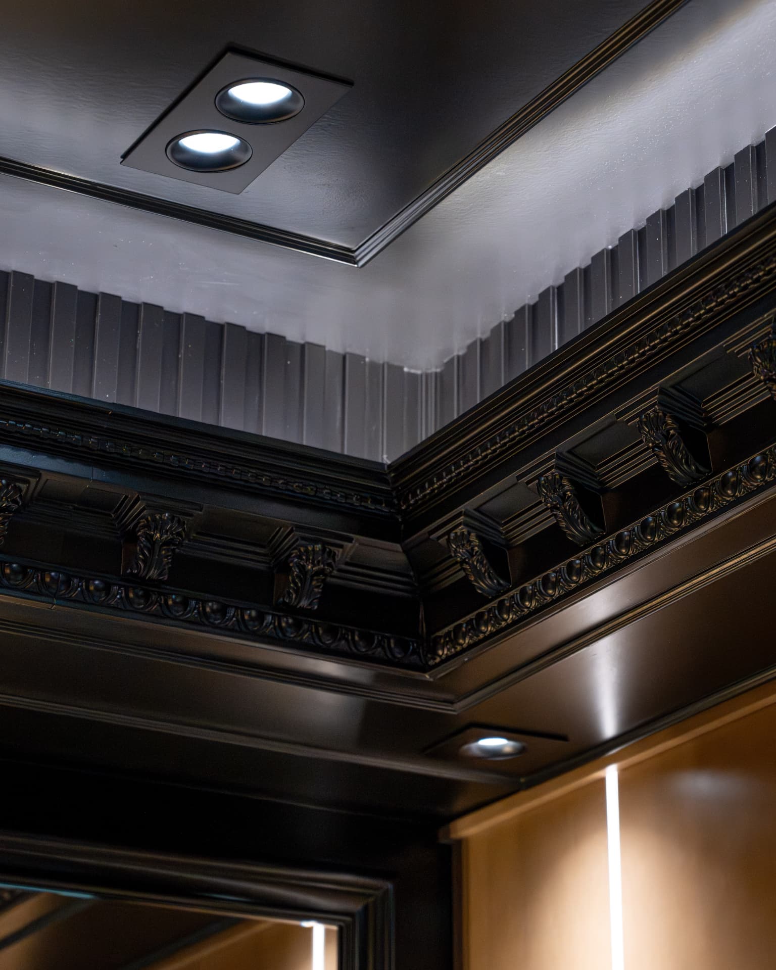 Detailed black crown moulding and fluted wall treatment beneath recessed lighting