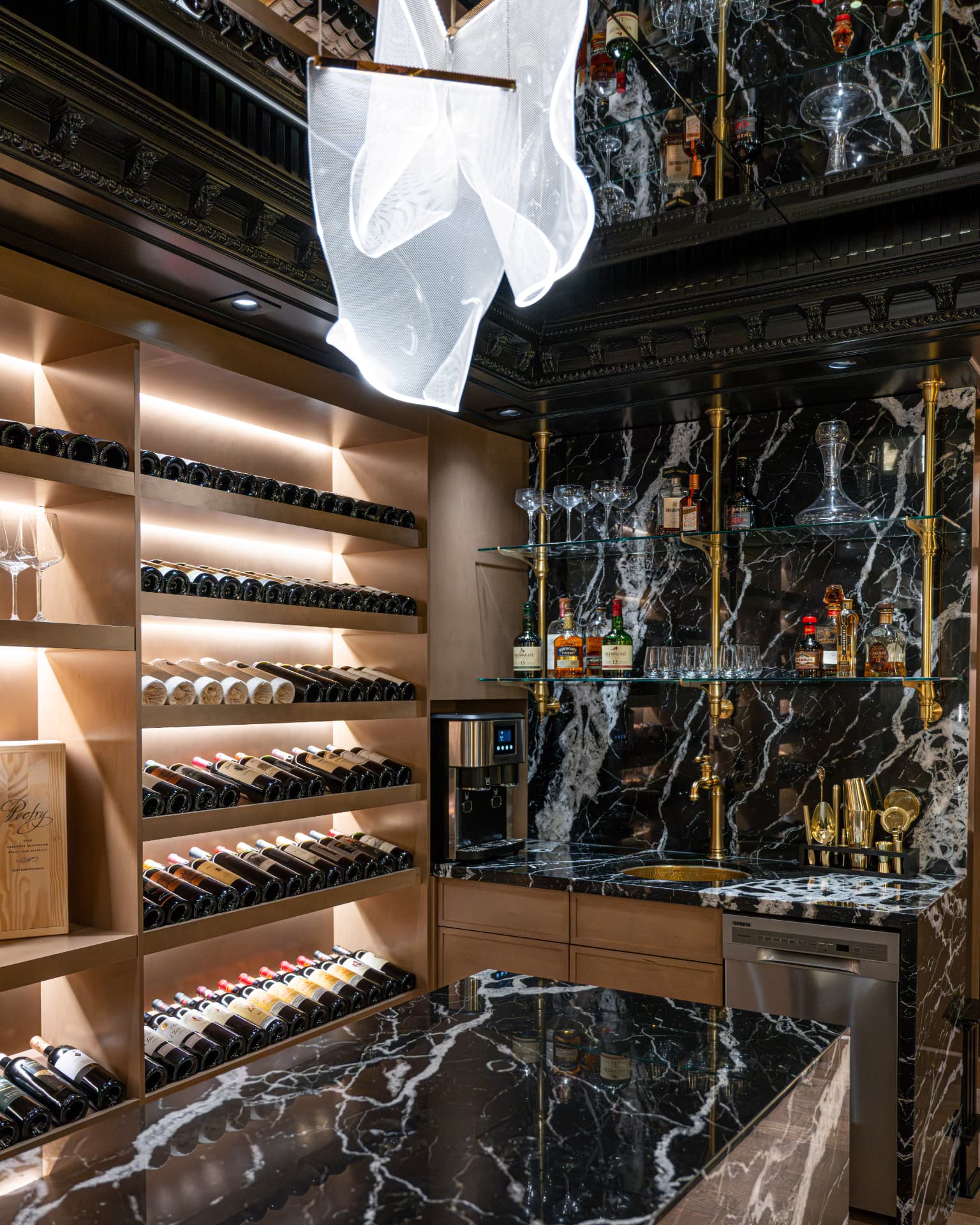 Bar with backlit wine racks, black marble counters, glass shelving, and brass fixtures