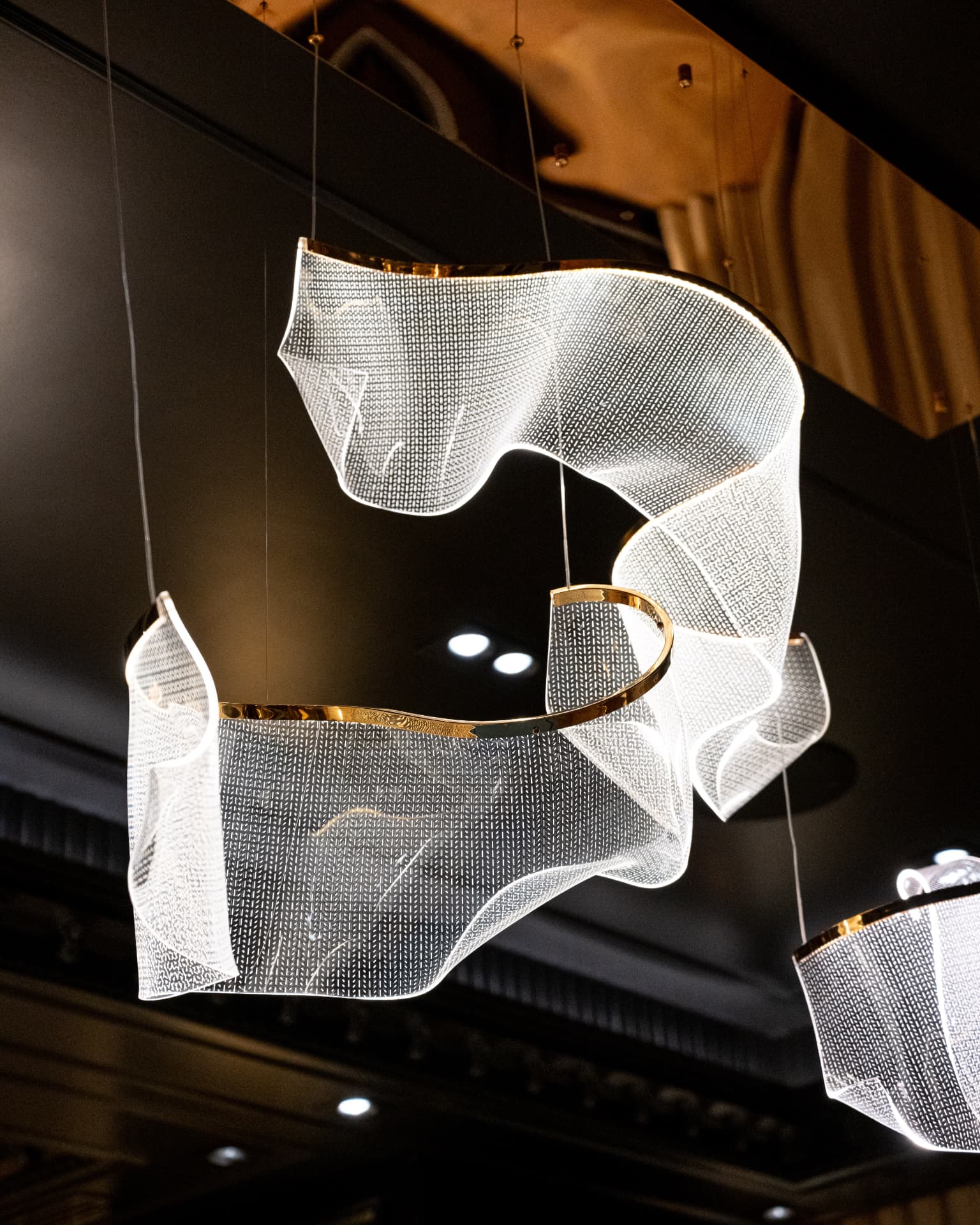 Sculptural layered chandelier with polished gold trim suspended beneath a dark coffered ceiling
