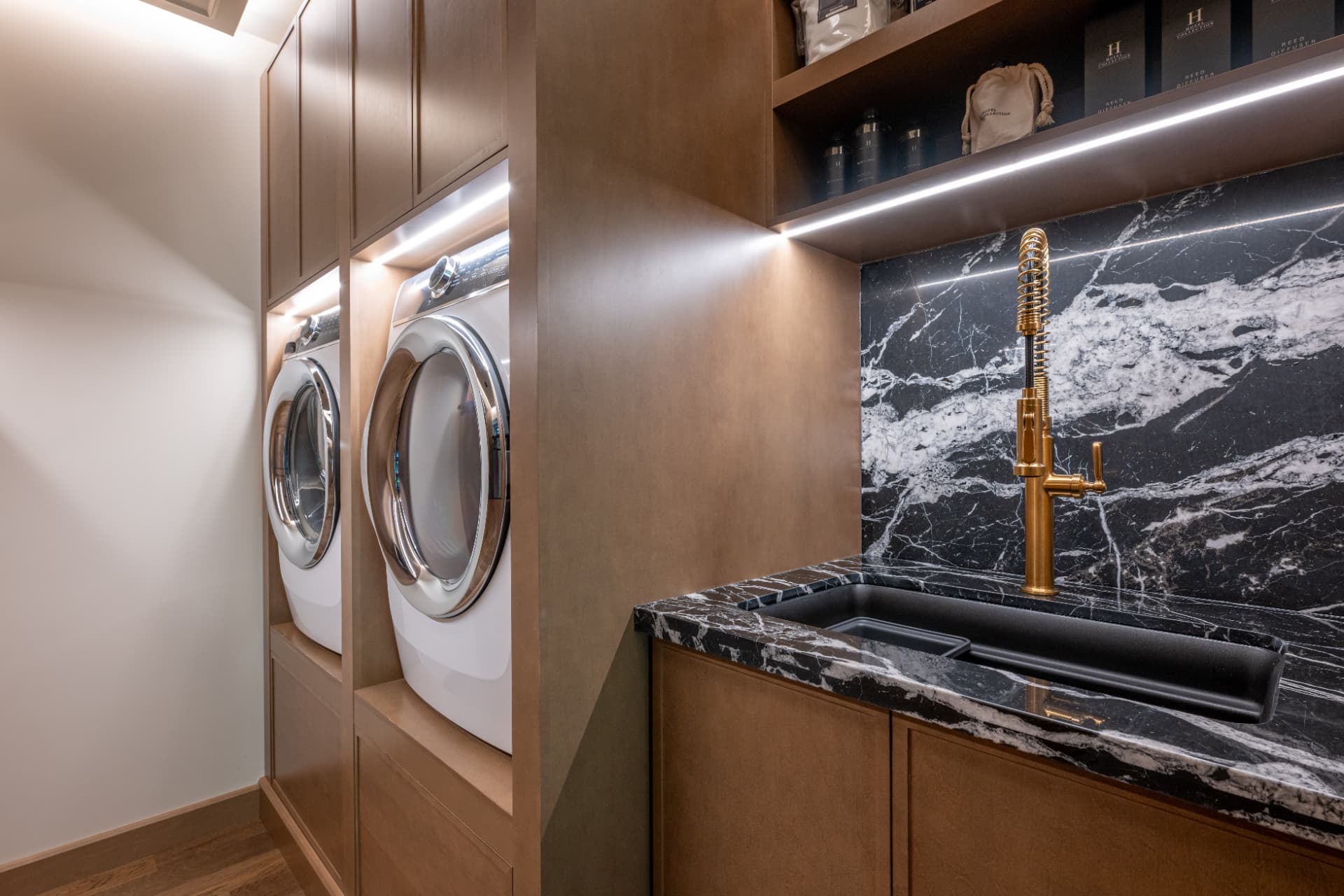 Custom laundry room with wood cabinetry, black marble sink, and brass faucet